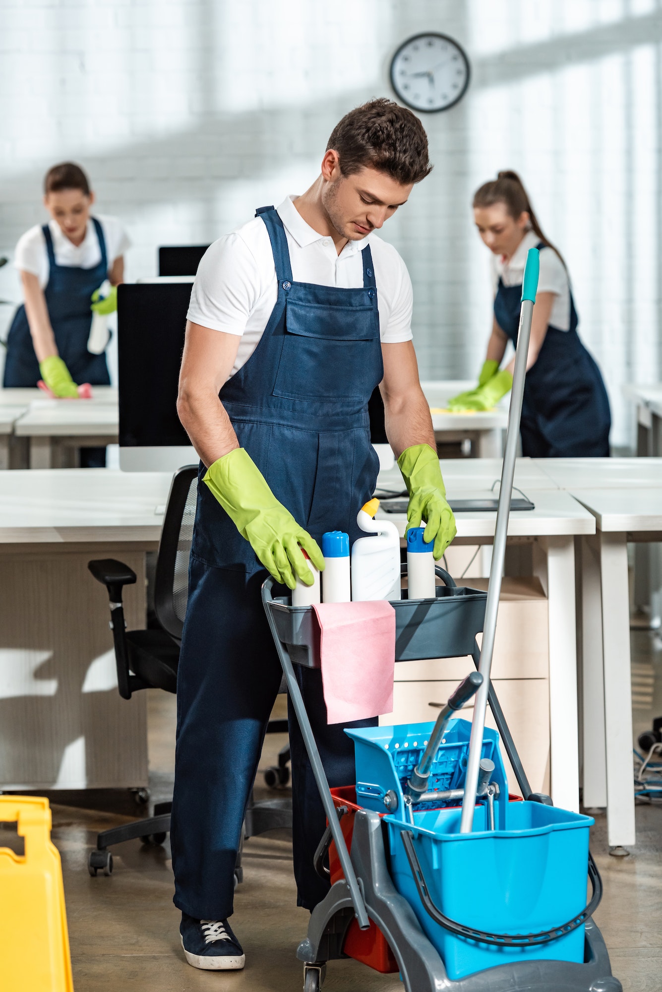 young-cleaner-standing-near-cart-with-cleaning-supplies.jpg